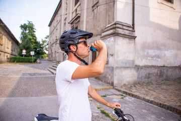 Portrait of a cyclist with a protective helmet on his head. He paused to drink the water from the...