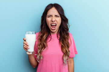 Young mixed race woman holding a glass of milk isolated on blue background screaming very angry and aggressive.
