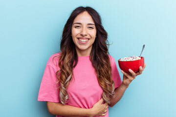 Young mixed race woman holding cereals bowl isolated on blue background laughing and having fun.