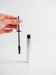 Women's hands hold the mascara open on a white background. A brush for applying mascara. The...