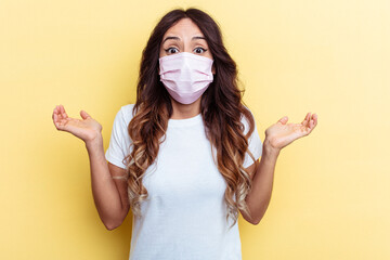 Young mixed race woman wearing a protection for virus isolated on yellow background shrugs...