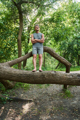Naklejka na ściany i meble Senior man standing arms crossed at the trunk of the tree and looking at the nature