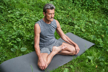 Naklejka na ściany i meble Caucasian mature man meditates while practicing yoga at the mat