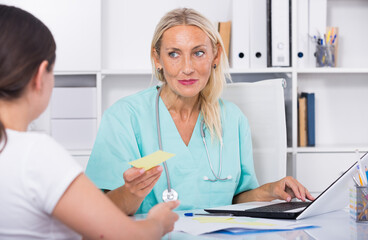 Fototapeta premium Female doctor working with patient in medical office and writing prescription