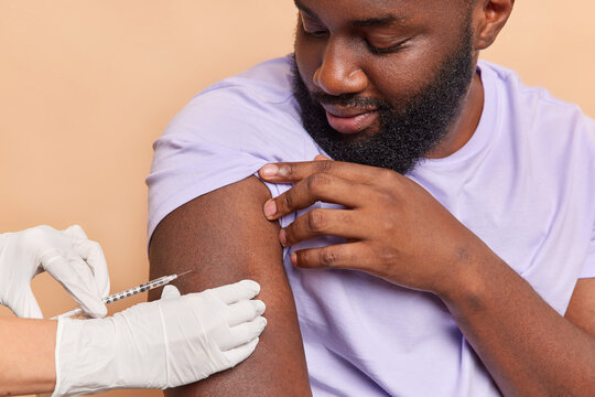 Nurse in white medical gloves makes vaccination in shoulder of patient. Dark skinned bearded adult man gets injection in arm protects himself from coronavirus Vaccine saves lives. Stop covid 19.