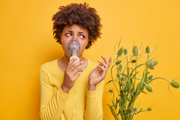 Unhappy young Afro American woman uses nebulizer for allergy treatment has asthmatic attack...