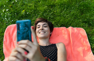 Attractive young female laying down on her towel and using her phone in the park while enjoying summertime in Hyde Park, London