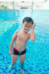 Cute asian kid cleaning ears after swimming in a pool