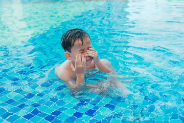 Foto op Plexiglas Child at the swimming pool steps, rubbing water from his eyes. © makistock