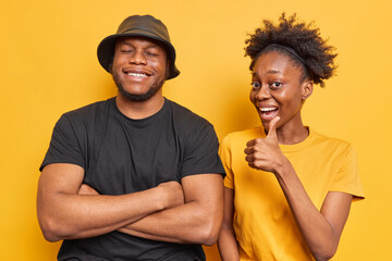 Studio shot of two cheerful dark skinned woman and man have fun smile happily show like gesture...