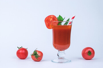 A glass of tomato juice and scattered tomatoes on a white background.