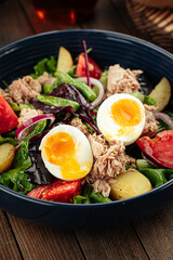 Tuna salad with eggs and vegetables on a wooden background