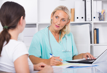 Portrait of mature female doctor listening to patient complaints at clinic