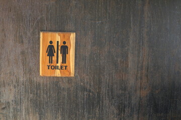 Toilet sign in wood frame on black painted metal wall. Some rusty and scratch on surface of wall.