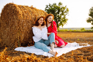 Two young woman in fashionable and stylish clothes posing near hay bales in the countryside. Fashion concept. Nature, vacation, relax and lifestyle.