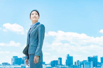 都心と青空を背景に立つ若いビジネスウーマン
