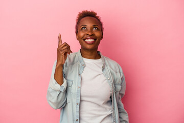 Young african american woman isolated on pink background indicates with both fore fingers up...