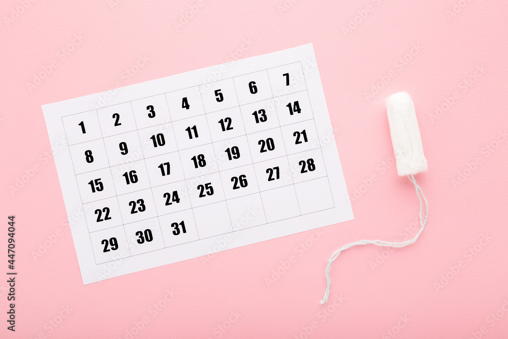 Wall mural White calendar and one tampon on light pink table background. Pastel color. Closeup. Female hygiene product. Menstruation cycle. Top down view.