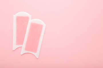 Two wax strips on light pink table background. Pastel color. Closeup. Female product for smooth body skin. Empty place for text. Top down view.