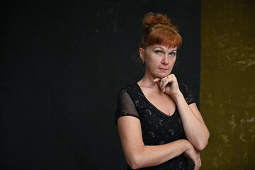 An adult Caucasian woman looks pensively into the camera with a smile. Portrait on a dark background