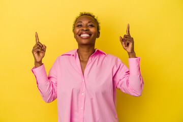Young african american woman isolated on yellow background indicates with both fore fingers up...