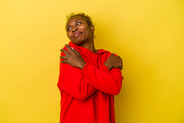 Young african american woman isolated on yellow background hugs, smiling carefree and happy.