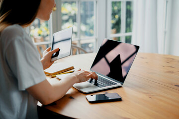 There is a laptop on the table and a tablet in his hands. A smart student does classes online via video link. Home training on the Internet network.
