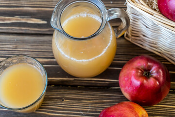 Red apples in a basket and apple juice in a jug on a wooden table