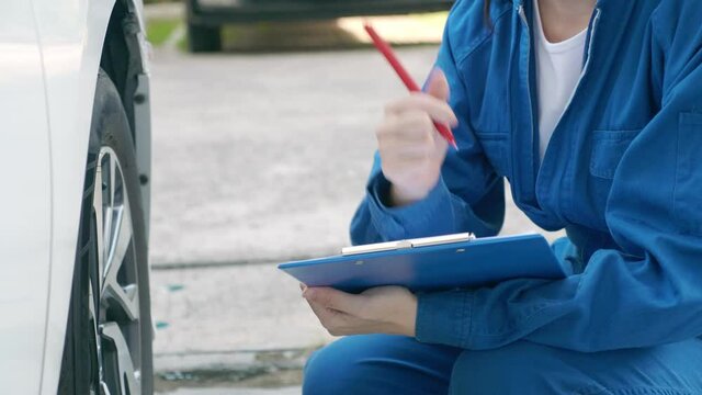 Low angle shot of unrecognizable female mechanic in blue jumpsuit uniform, holding checklist and pen, evaluating tire condition, writing, putting thump up. Engineer and car maintenance service concept