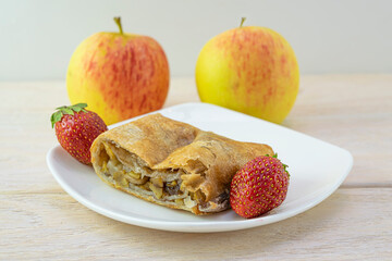 A piece of apple strudel with cinnamon in a white plate with strawberries close-up
