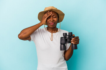 Young african american woman holding binoculars isolated on blue background being shocked, she has remembered important meeting.