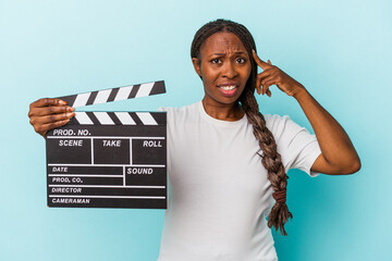 Young african american woman holding clapperboard isolated on blue background showing a...