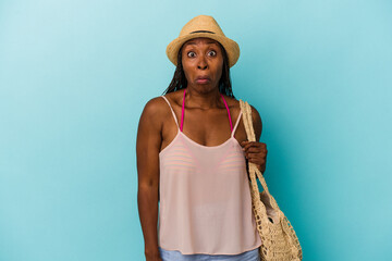 Young african american woman wearing summer clothes isolated on blue background shrugs shoulders...