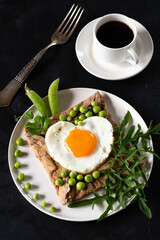 Galette bretonne with egg, arugula and green peas on a black background. Coffee in a white cup.