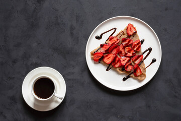 Galette bretonne with strawberries and balsamic sauce on a black background. Coffee in a white cup.