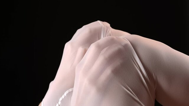 Footage of female hands under white tights on black background