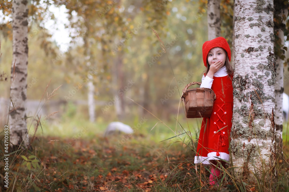 Wall mural A little girl in a red hat and dresses is walking in the park. Cosplay for the fairytale hero 