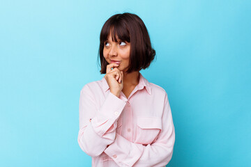 Young mixed race woman isolated on blue background relaxed thinking about something looking at a copy space.