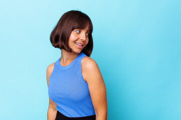 Young mixed race woman isolated on blue background laughs happily and has fun keeping hands on...