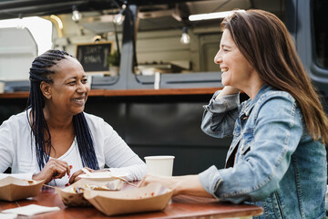 Multiracial women eating at food truck restaurant outdoor - Focus on african woman face