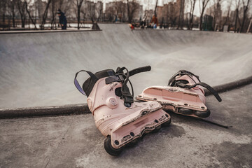 Pink dirty rollers lie on the edge of a ramp in the skatepark of the metropolis on a sunny spring /...