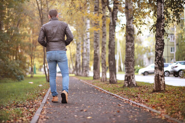 Fototapeta premium Autumn concept. A man walks through the city. Autumn leaves on the footpath.&nbsp;