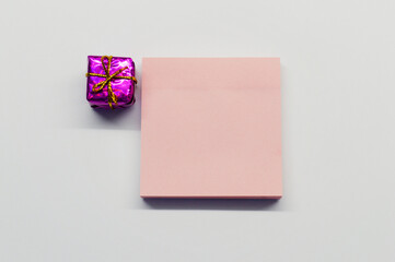 Pink shiny little gift and paper for notes on white background