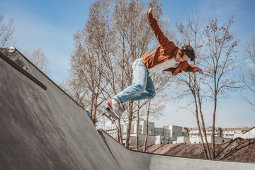 Guy preparing for competitions in extreme sports is focused on jumping from a ramp in a skatepark, carefully monitoring the correctness of performing tricks on a skateboard. Skatepark of a metropolis