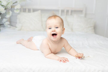happy smiling baby in diapers on a white cotton bed at home six months old