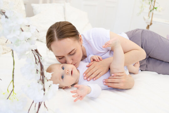 portrait of a mother with a baby, a mother kisses a child and gently hugs him on a white bed at home, maternal love and care
