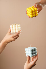 Three female hands holding yellow, blue and white bubble candles on beige background