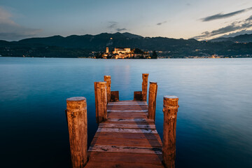 Orta San Giulio / Italy - June 2021: The island of San Giulio with a wooden pier in the foreground at sunset (blue hour), long exposure