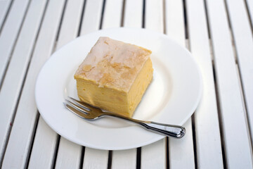 Piece of vanilla custard cream cake with fork on the plate on the table