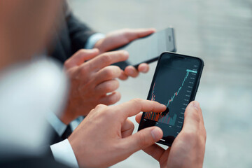 Growth charts on stock markets. Male brokers hold phones in their hands. Cryptocurrency trading on the stock exchange